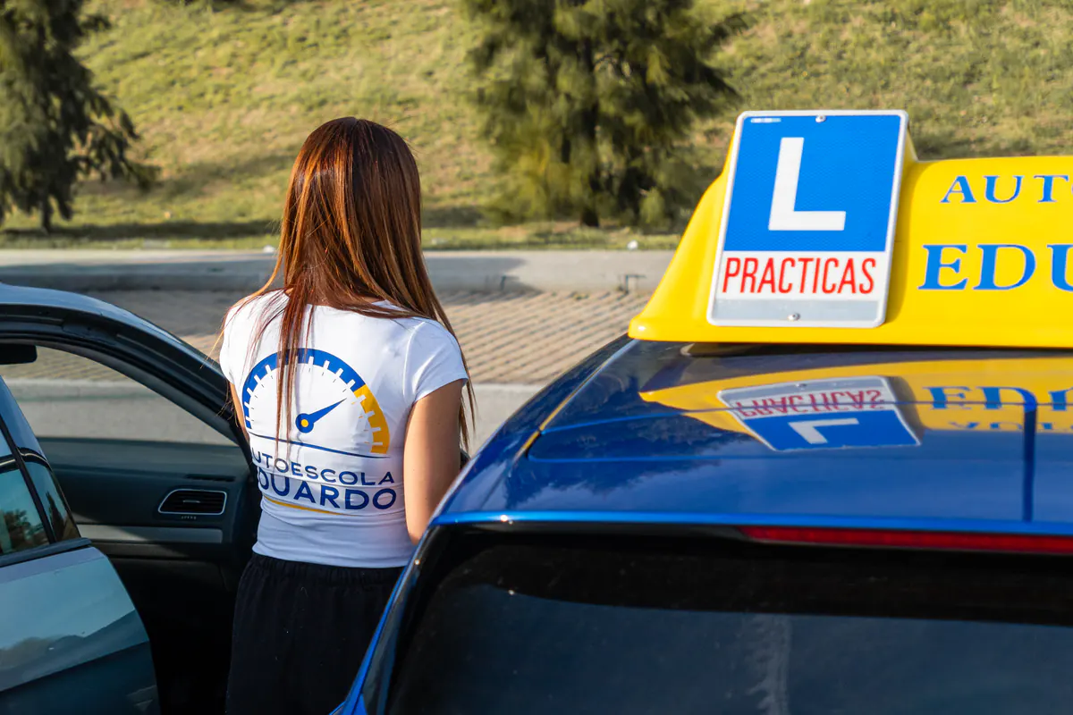 Profesora junto al coche de prácticas con el rótulo L en el techo