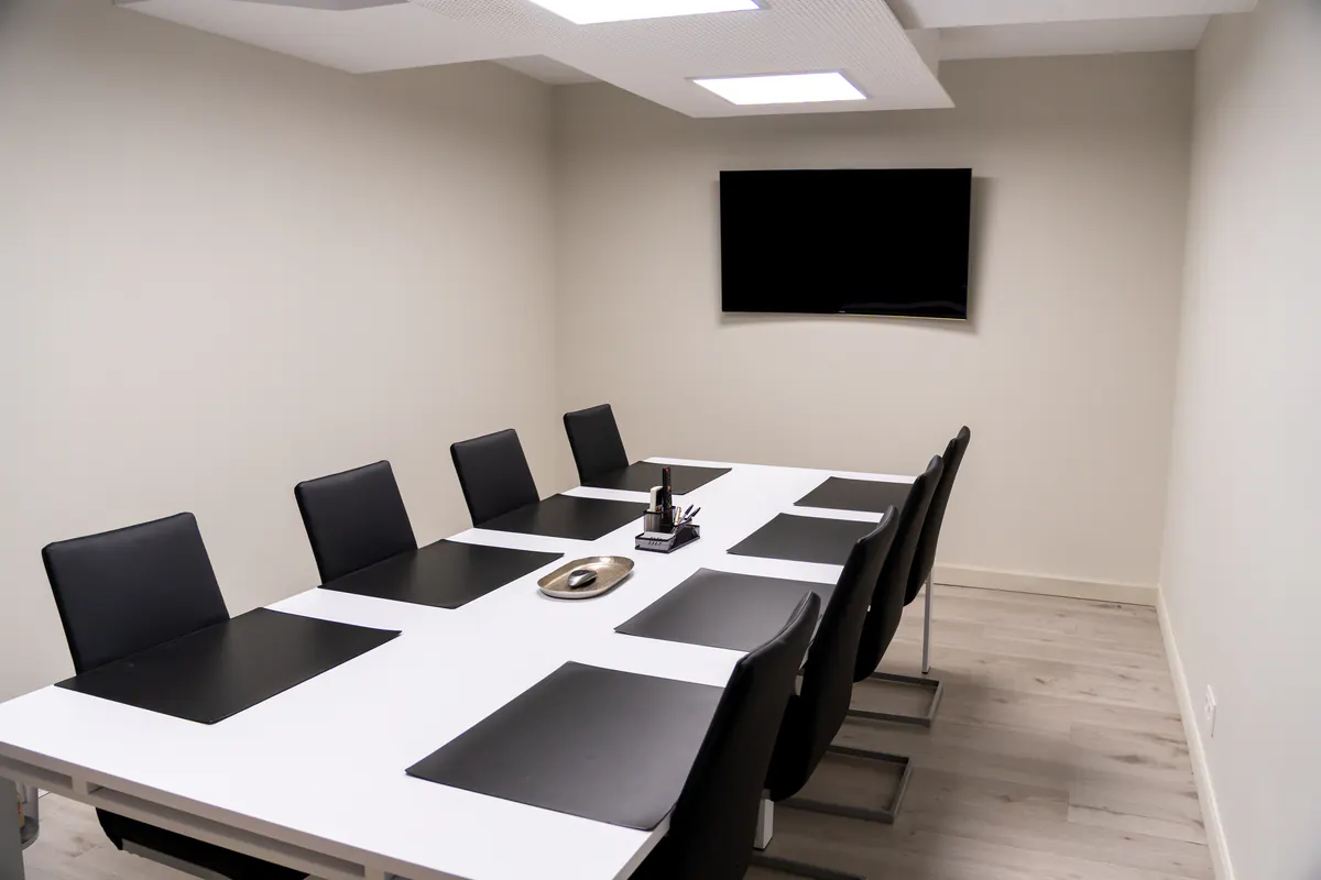 Sala de reuniones del despacho con mesa blanca y sillas negras