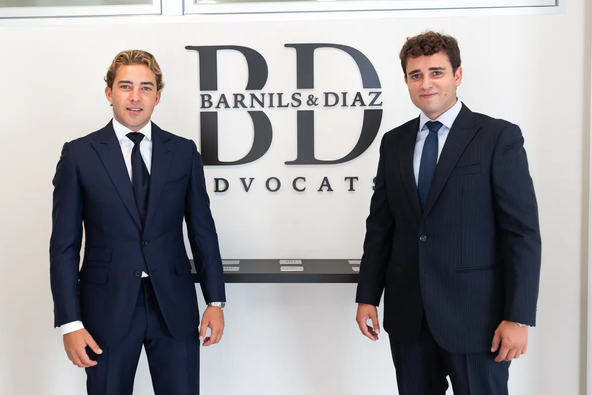Los socios de Barnils & Díaz junto al logotipo del despacho