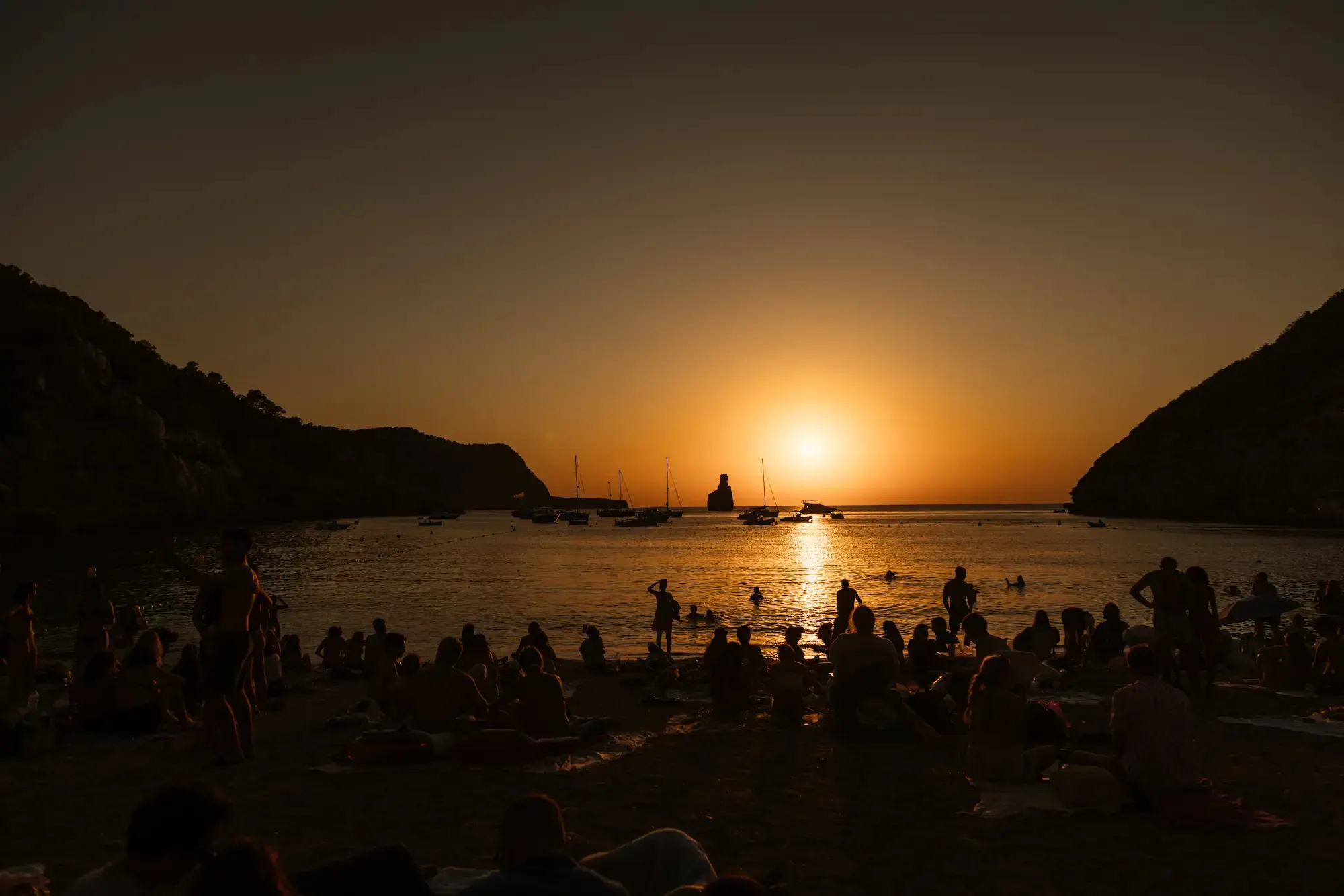 Atardecer en Cala Benirràs, con el sol sobre el mar y siluetas en la playa