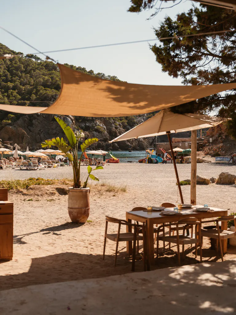 Mesas del restaurante bajo las velas, con la playa de Benirràs al fondo
