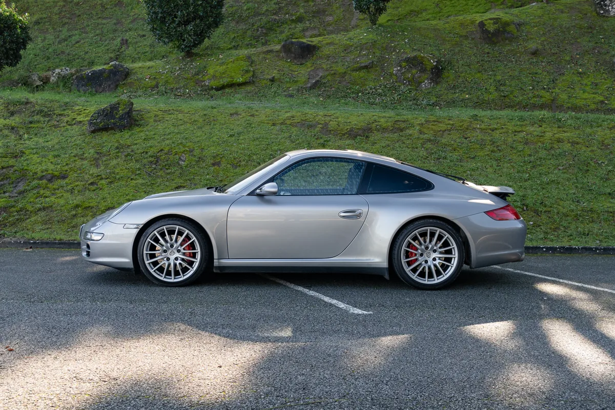Porsche 911 997 Carrera 4S plateado de perfil junto a un talud de hierba