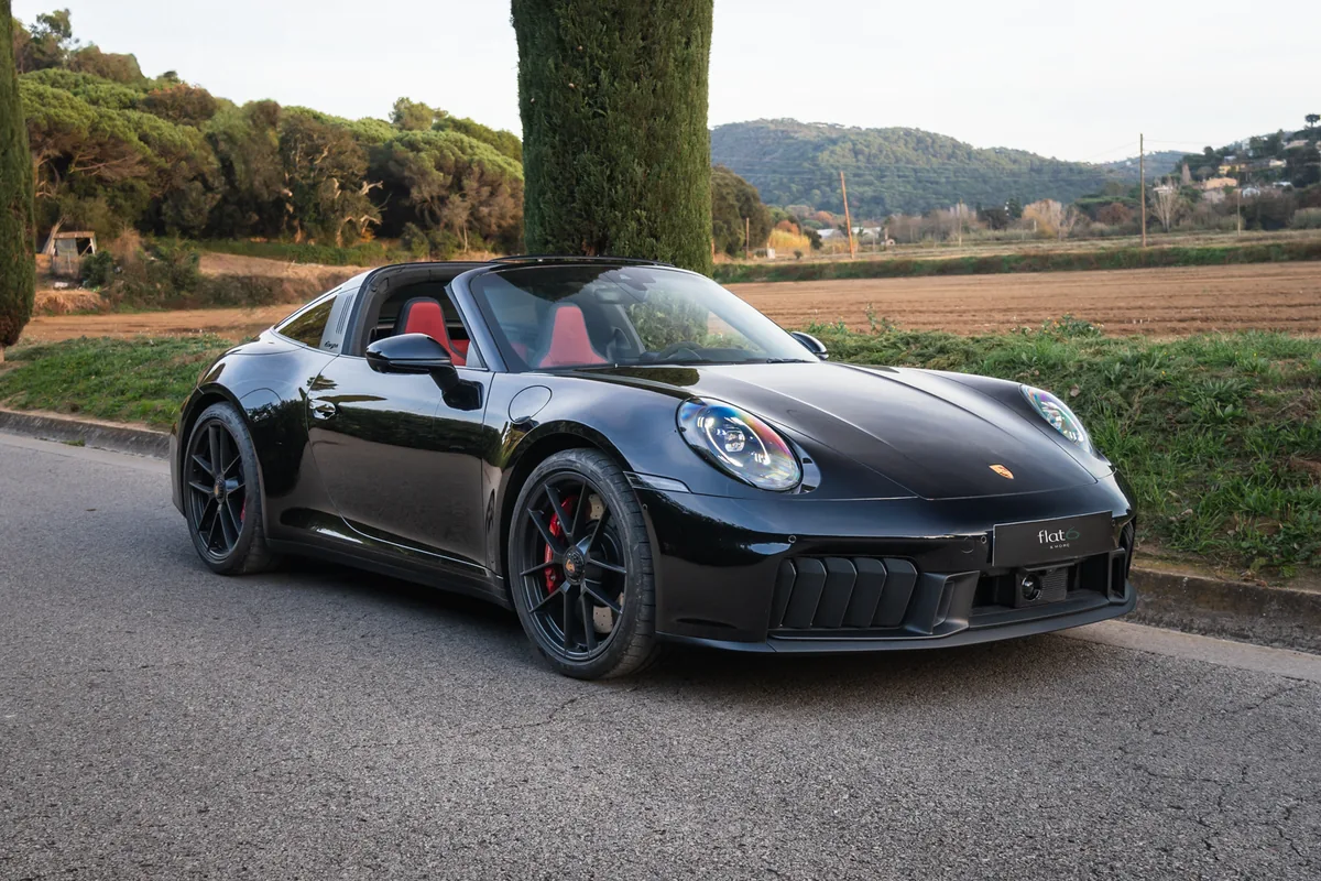 Porsche 911 Targa negro con el portamatrículas de Flat6, en un camino entre campos