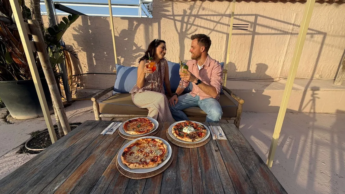 Pareja brindando con pizzas de Forno di Marea en la terraza al atardecer