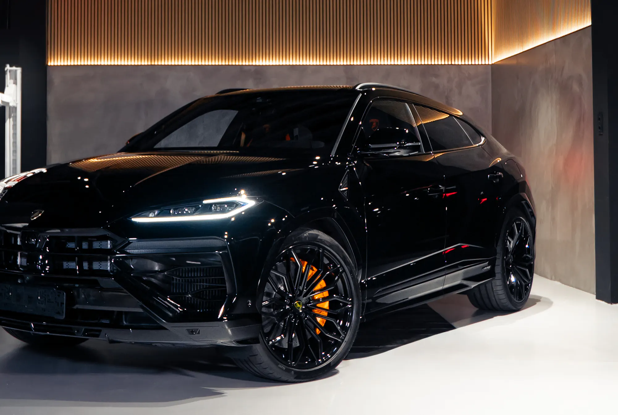 Lamborghini Urus negro en el showroom de Maison Automotive, con la pared de madera iluminada