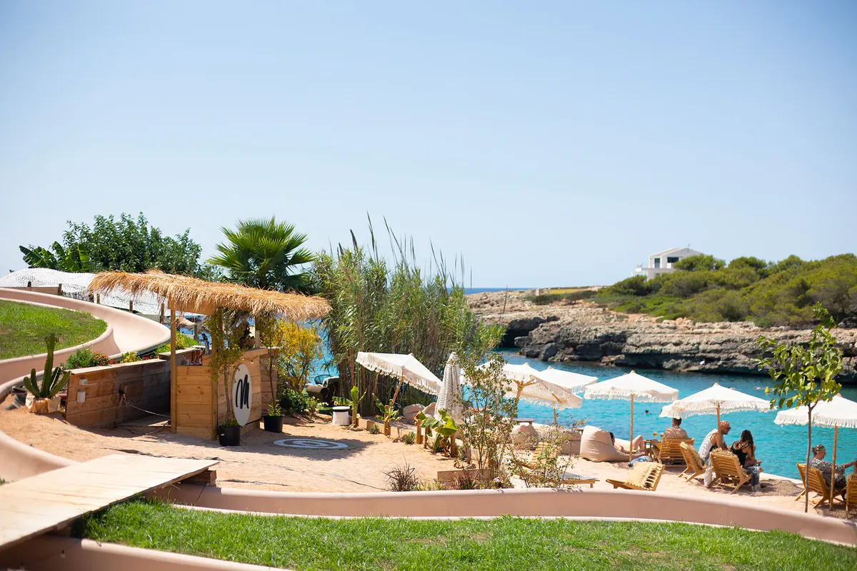 Jardín del beach club de Marea con sombrillas y la cala al fondo
