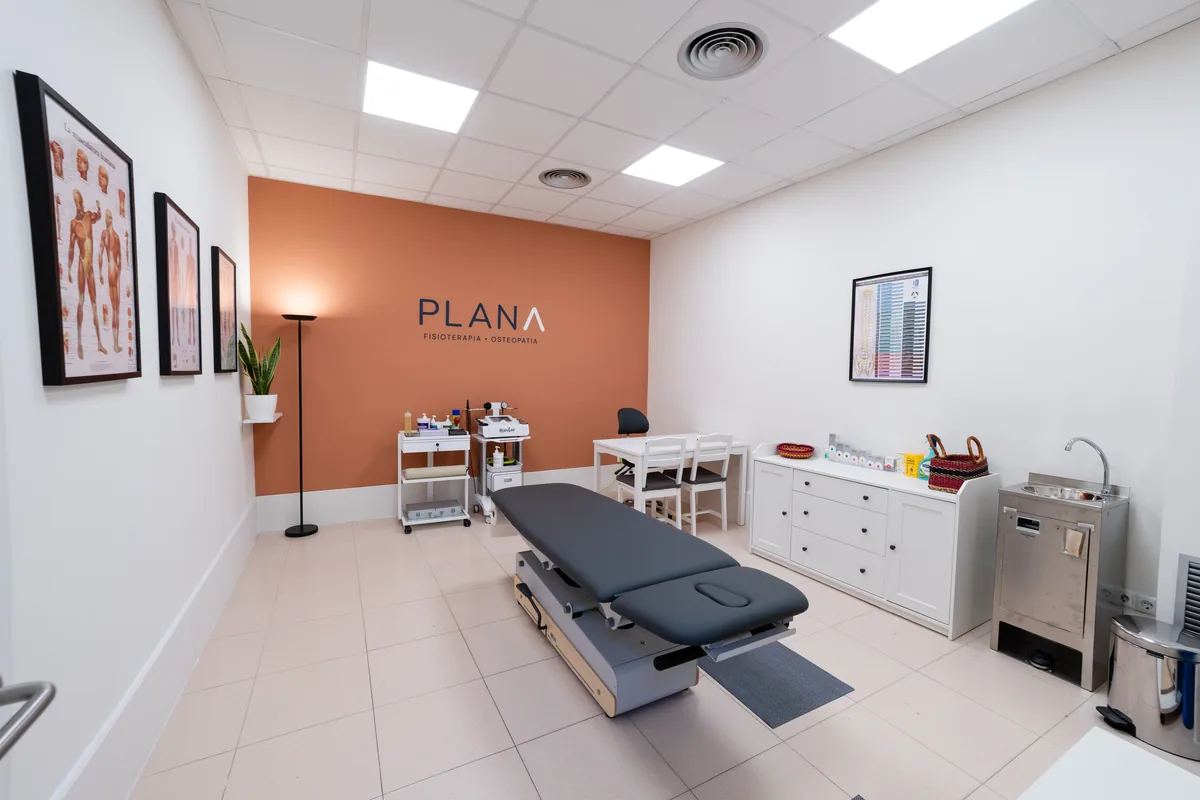 Sala de tratamiento de Plana Fisio con la camilla y el logotipo sobre la pared coral