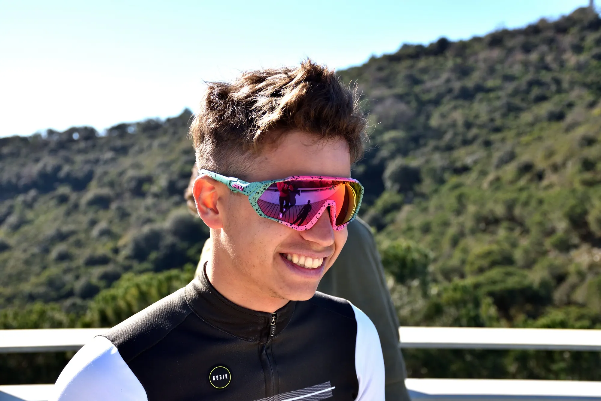 Ciclista sonriendo con gafas Vairok de lente rosa en un mirador de montaña